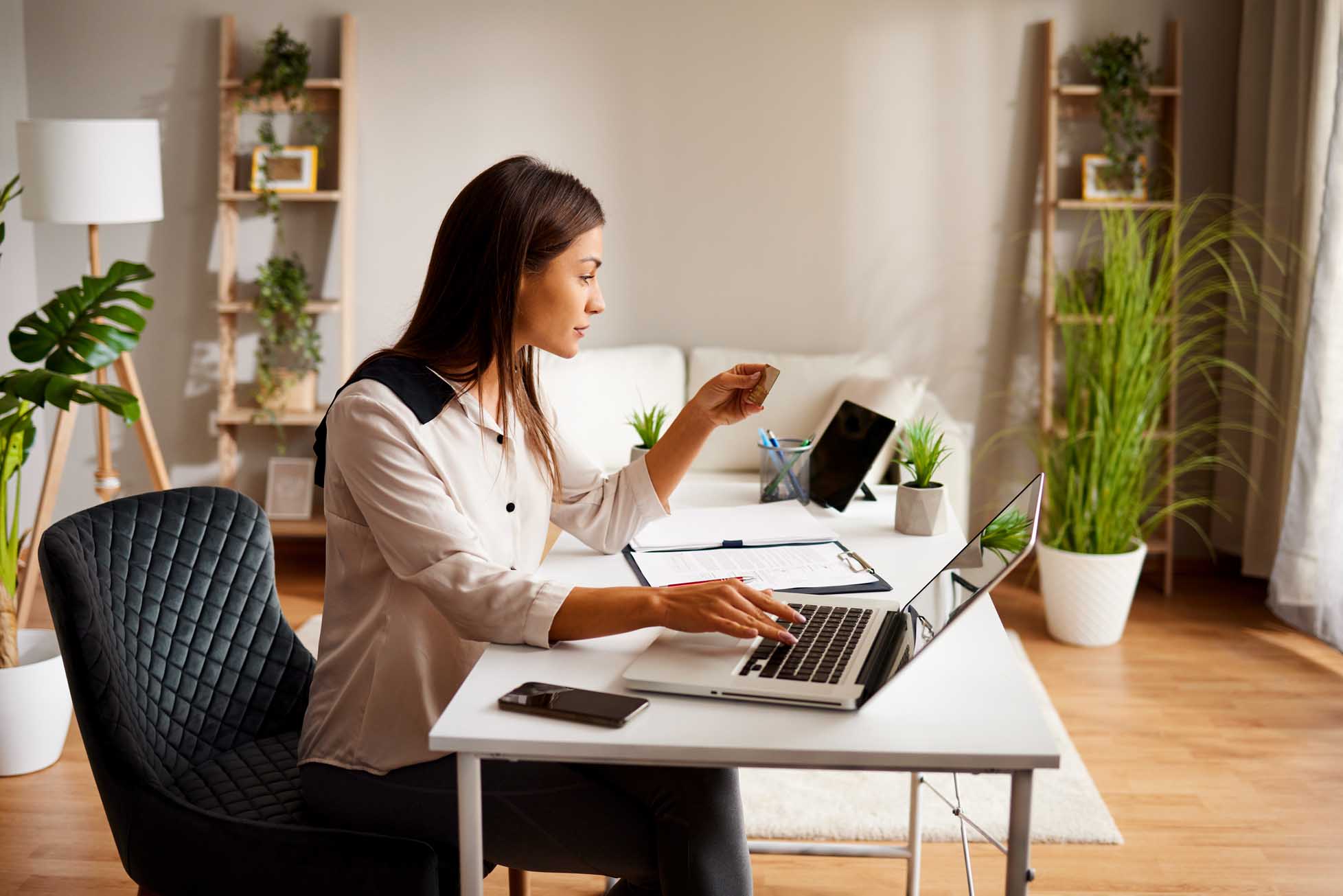 Portrait of young woman paying bills with credit card and laptop in office