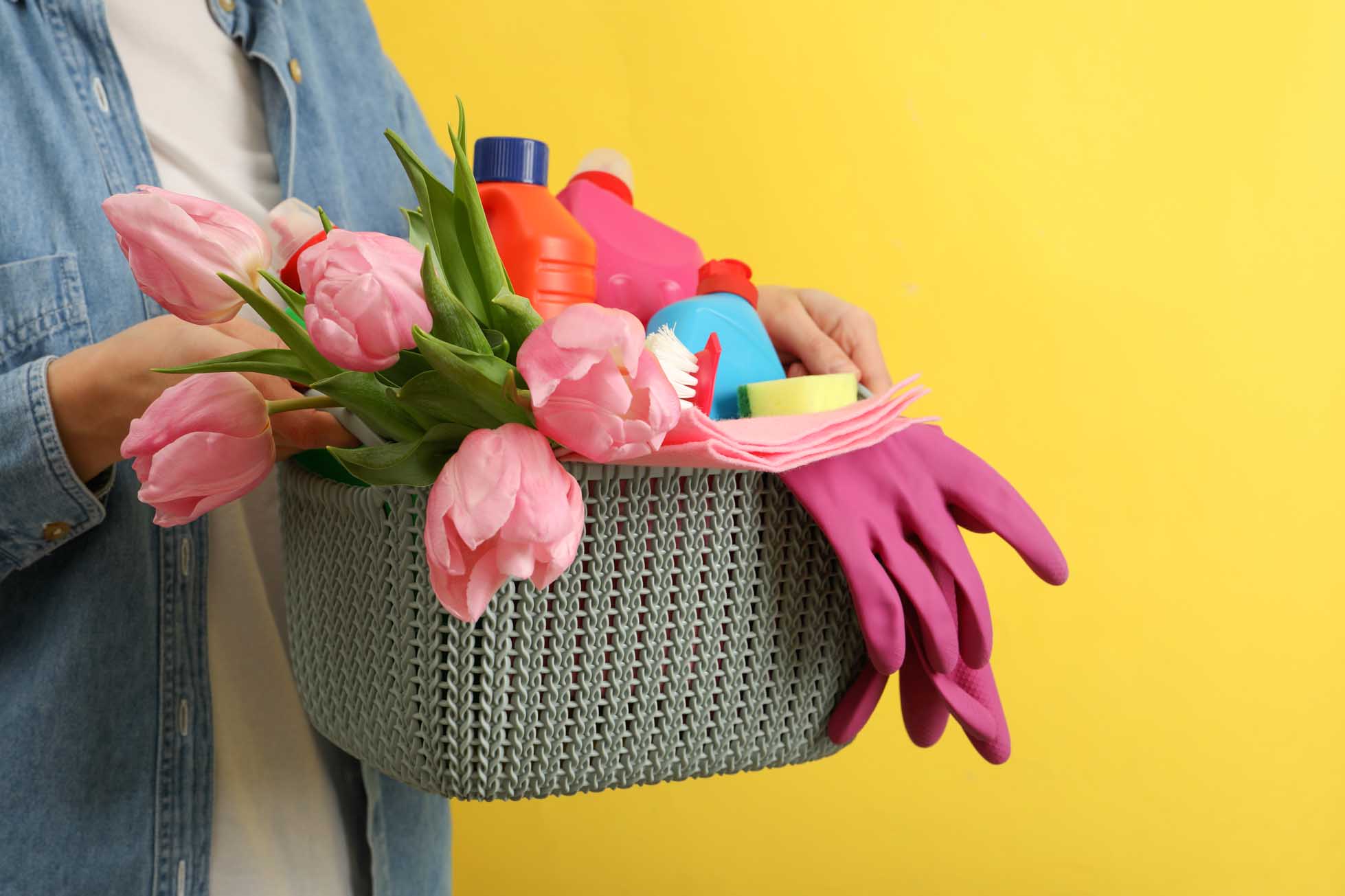 Woman hold basket with cleaning tools on yellow background